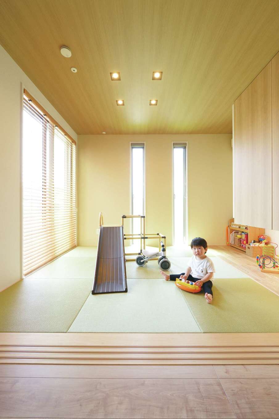 丸昇彦坂建設【デザイン住宅、子育て、間取り】奥さまの両親が泊まりに来ることも考えて、LDKに続き間の和室を配置。3方向に窓を設け、明るく開放的な空間に。現在はキッズコーナーとして活躍し、地窓の上の吊戸棚にはおもちゃをたっぷり収納。デッキにも直接出入りでき、子どもがのびのびと遊ぶことができる