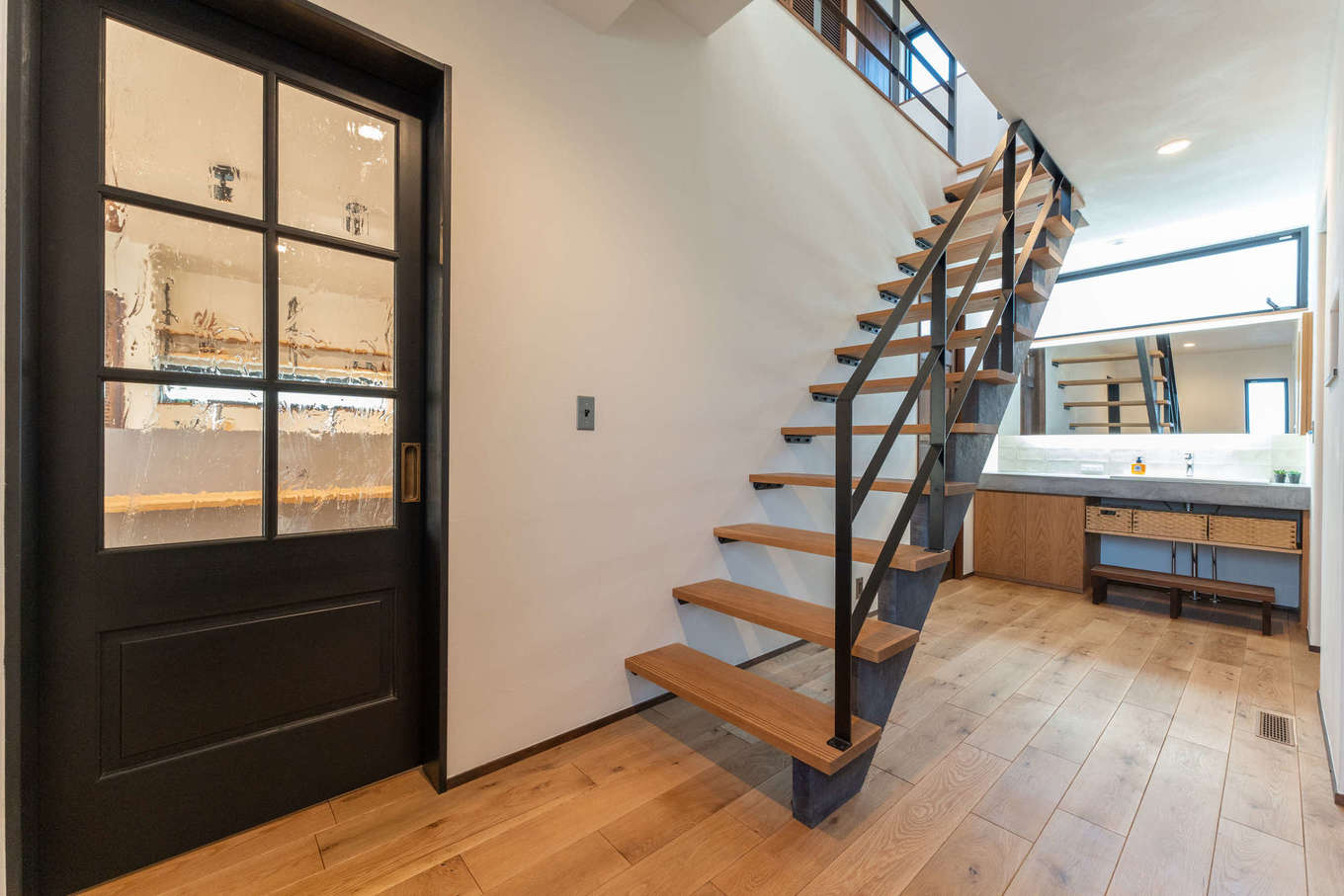 バルハウス【デザイン住宅、自然素材、間取り】スケルトンの鉄骨階段の向こうに視線が抜ける、明るくて開放的なホール。重厚感のあるリビングドアは造作によるオリジナルで、アンティークガラスがおしゃれのポイントだ