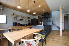 ナチュラルモダンな印象の室内。ダイニング・キッチンの頭上は木製パネルを貼って、視覚的に空間をゾーニングすることを狙った。ダークカラーのオープンキッチンは、広々とした天板で料理がしやすい。奥に見えるスケルトン階段の色みとよくマッチしている