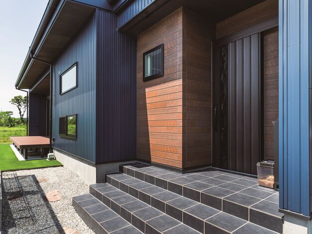 重厚な雰囲気のエントランス。ブルーのガルバリウムの外壁に木目調が映えます。