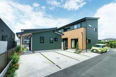 モスグリーンのガルバリウムが青空に映える外観。左の平屋が同時に新築したお姉さまの家