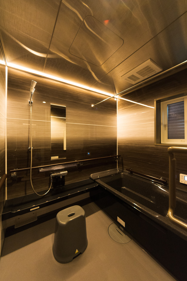 イーホーム【収納力、二世帯住宅、屋上バルコニー】ステンレス天井とLEDのライン照明を付けた浴室。浴槽まで手すりに沿って歩ける配慮も