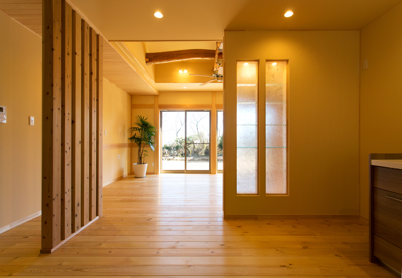瀧口建設｜リビング北側のキッチンは通風と採光に工夫を。杉のつけ柱は玄関からの視線を遮り風は通してくれる。飾り棚の壁には透過性のあるパネルを使い、リビングから光を採りこんでいる