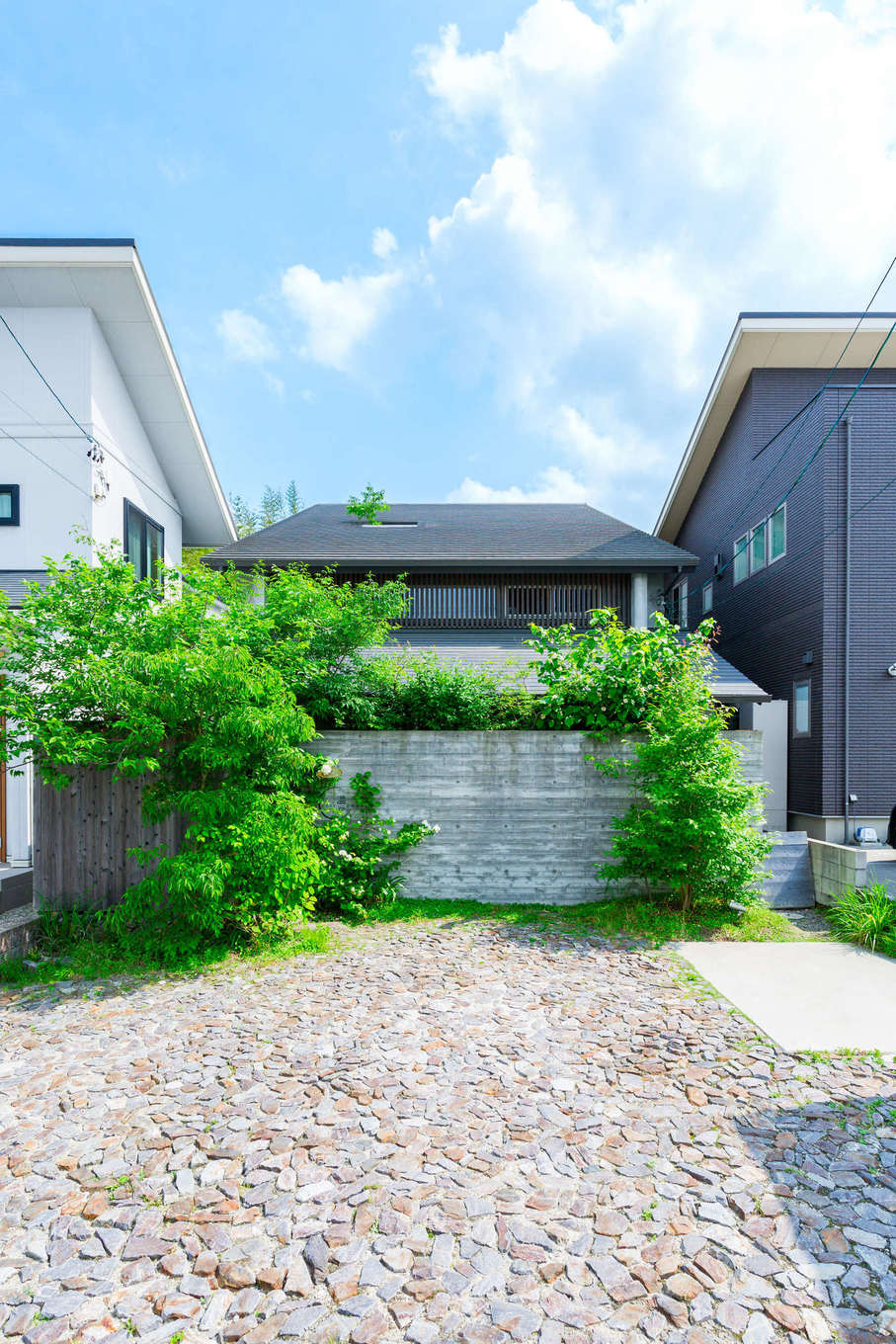 温戸ライフ【自然素材、間取り、インテリア】もともとそこに建っていたかのように、街の景色に馴染む外観。両隣に家が迫っているものの、視界の開けた南側からたっぷりの光と風を取り込むかたちに仕上げている。木目調のグレーの壁は、コンクリートに木板を貼り付けてから剥がしたもの