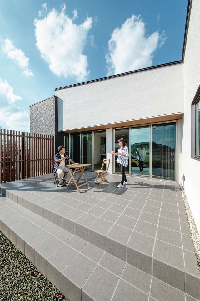 吉川住建【デザイン住宅、夫婦で暮らす、平屋】リビングとつながるタイルデッキはなんと14畳。休日は朝からテーブルと椅子を出して、食事やカフェタイムを楽しむ。世の中が落ち着いたら、友達を大勢呼んでBBQをする予定。春には目の前の公園に鮮やかな桜が咲き誇る