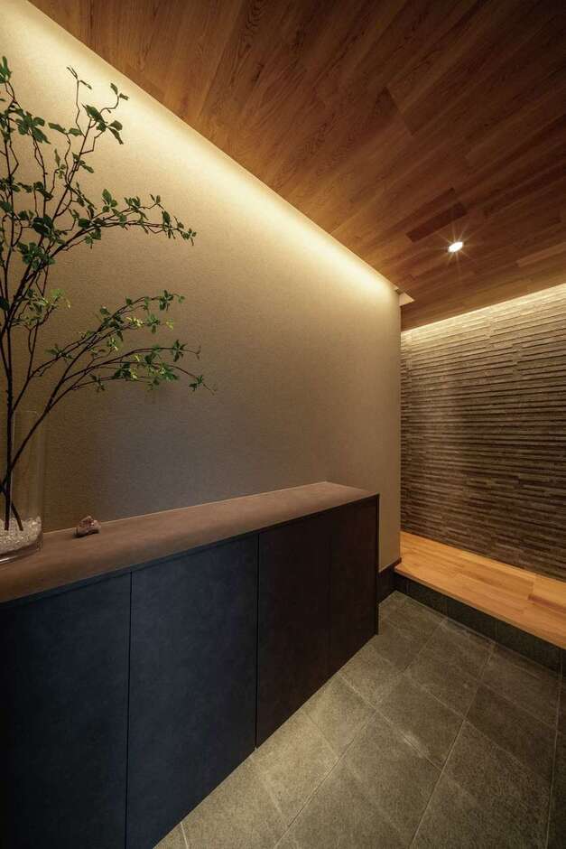 天井のナラ、正面のエコカラット、目に優しい間接照明により、帰宅をあたたかく迎える玄関に。おでかけグッズや上着を収納するクローゼットが近くに設けられている