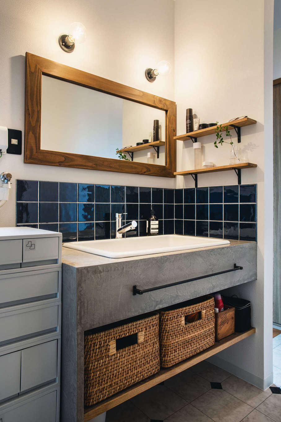 ALAIN（アラン）｜造作の洗面台はモルタルのような質感で、防水性の高いMORART（モラート）を採用。マットな仕上げの中に微妙な光沢感を持ち、柔らかい陰影による奥行きのある表情を演出する。1日1工程で、4日間かけて製作した。ワイドな鏡、ダークブルーのタイル、アイアンの取っ手とのバランスが美しい