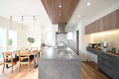 ペニンシュラキッチンは天板もキャビネットもグレーで統一し、ポップアップ天井と上部の収納を木目にすることで、木の温かみとモノトーンの無機質な素材感がバランスよく調和した。キッチンの奥にはパントリー、ダイニングの壁面にはスタディコーナーも確保