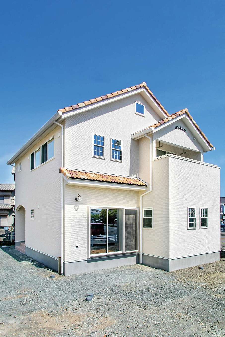 モチケン【デザイン住宅、自然素材、間取り】白い壁に赤茶系ミックスの屋根瓦が映える外観。西側は小さい窓を高所に配置し、通気を取りつつ周囲からの視線を避けた