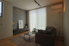 モダンなリビングルーム。天井と同じ高さの大きな窓から自然光が入り、落ち着いた雰囲気を醸し出している。シンプルなインテリアが空間を引き立てている。