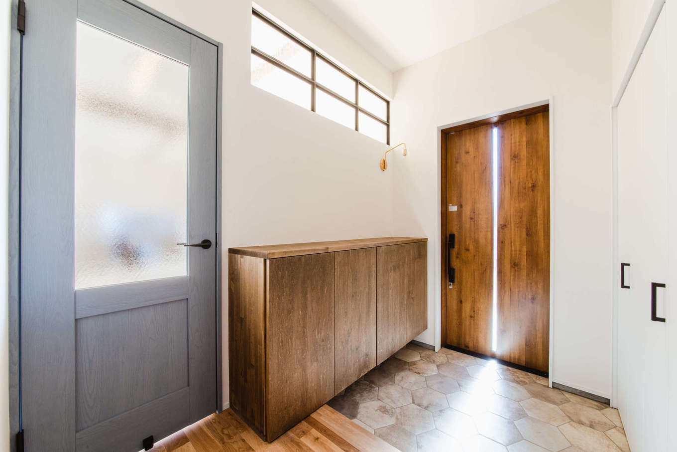 Select工房【デザイン住宅、間取り、平屋】玄関ホールは、リビングからの明かりを取り入れる室内窓やガラス入りのドアを採用。ドアの色も空間のアクセントとなっている