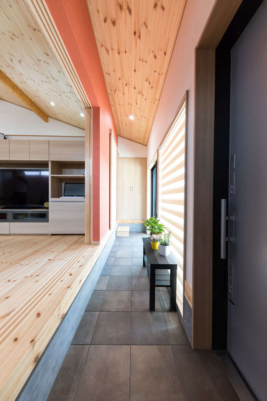 建築システム（狭小住宅専門店）【1000万円台、自然素材、平屋】玄関土間からそのままリビングへ上がる。土間はキッチンまで続いているので、買い物帰りの奥さまにも優しい動線。壁は木の風合いに合う明るいえんじ色に。窓の外の軒天井にも同じ色を採用している