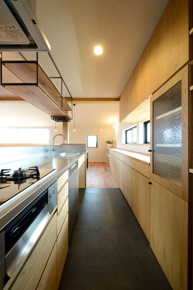 石牧建築【デザイン住宅、二世帯住宅、建築家】オリジナルのキッチンと収納棚。年に数回、親戚が25人程集まる機会があるため、ミーレ社製の大型の食洗機を採用した。オリジナルの吊り棚にはワインバーのようにワイングラスを吊るしておけるようになっている