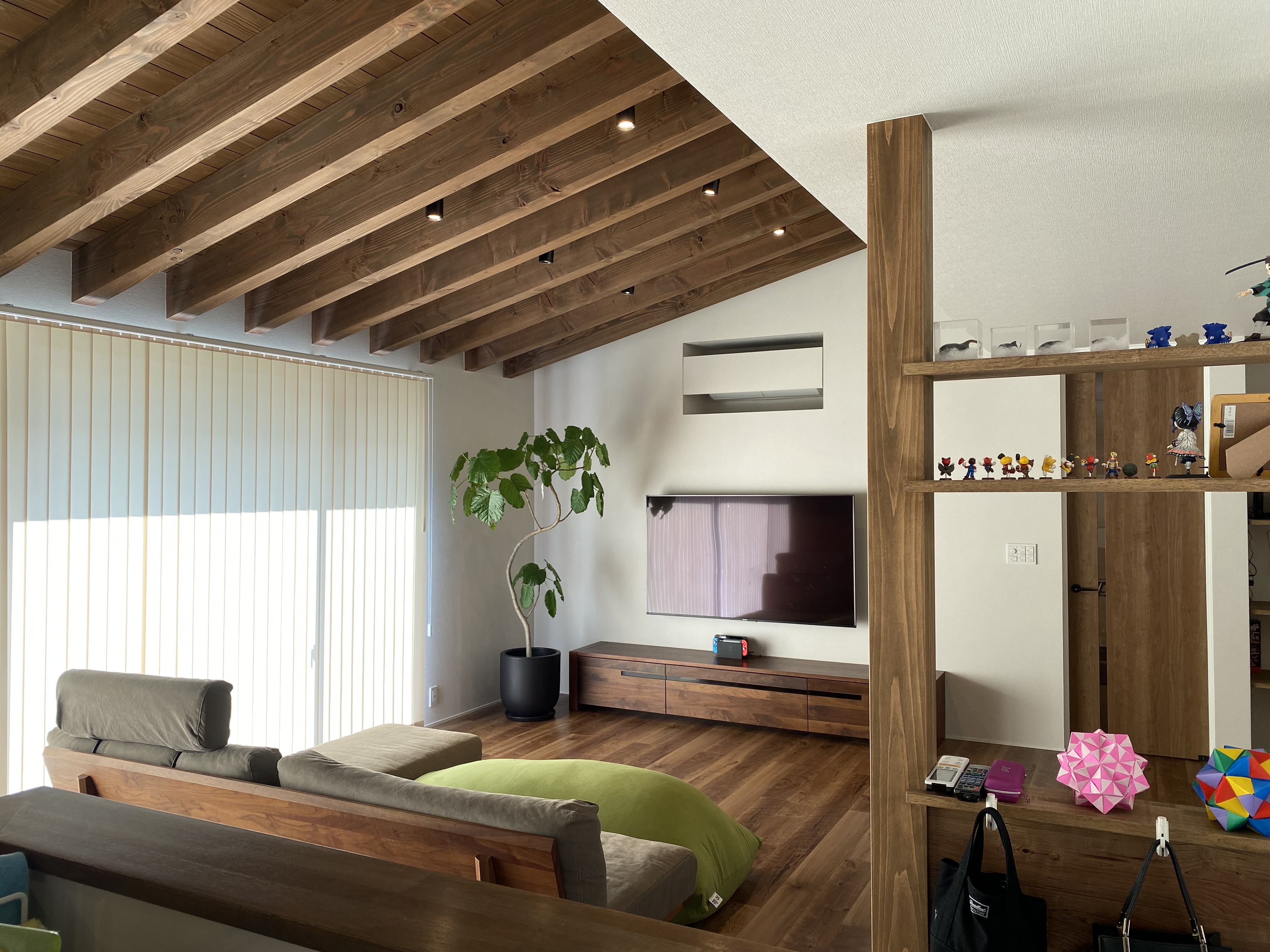 安田住宅｜安田建築設計室｜垂木あらわしが特徴的なリビング。植物と調和し、自然素材と温かい雰囲気が感じられる空間。壁面にはテレビボードが設置され、実用性も兼ね備えている。
