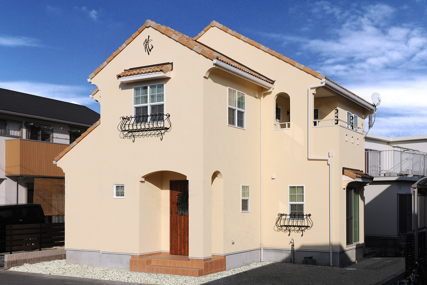 アイディートゥー 一級建築士事務所【デザイン住宅、輸入住宅、間取り】ルージュブラウンの洋風瓦とアースカラーの外壁が、青空に映える外観。アイアンの妻飾りやフラワーボックスを配した、南欧風スタイルが特徴的