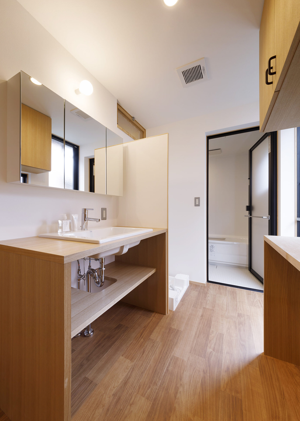 灯建築舎【デザイン住宅、自然素材、省エネ】造作による洗面台と収納が、空間の統一感とともに利便性をもたらす。カウンターは、下部に洗濯物のカゴを置ける高さに。洗濯物を物干し場まで最短距離で運べるよう、勝手口を用意。洗面脱衣室やトイレにも「びおソーラー」の吹き出し口があり、温度差が少ない環境で過ごすことができる