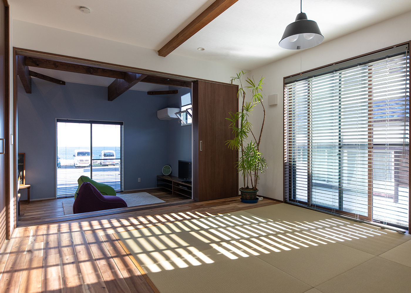 小玉建設【自然素材、夫婦で暮らす、平屋】小上がりの段差は、ソファ代わり。腰を下ろせば、道路と駐車場をはさんで正面にキラめく海が広がる。和室はL字型に板張りにしたことで、椅子やグリーンを置くことができる上、玄関からの通路としても機能している