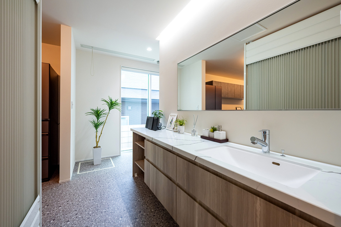 広々とした洗面スペースで、明るい照明と大きな鏡が使いやすさを演出している。清潔感溢れる木目調の収納が、空間に温かみを加えている。