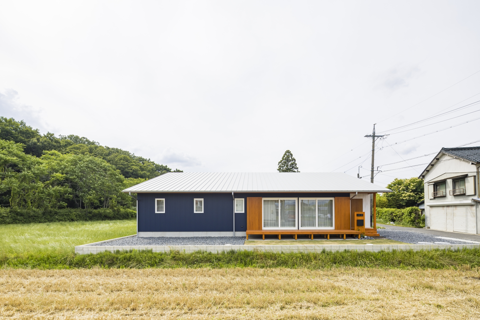 KANAZAWA STYLE/金澤建築【省エネ、間取り、平屋】自然豊かで、子育て環境に恵まれたロケーションに佇む平屋のA邸。外観は、ブルーの外壁にグレーの大屋根がバランスよく調和している。建物を真南ではなく、やや南東にずらして配置し、なおかつ軒を深く伸ばすことで、効率よく日射取得と日射遮蔽が可能に
