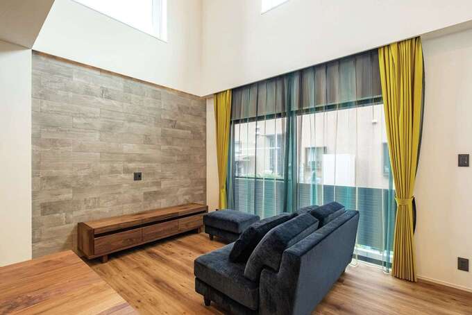 TVボードの背面はエコカラットで高級感を演出。ソファとレースカーテンはドアの色に合わせ、からし色のカーテンがアクセント