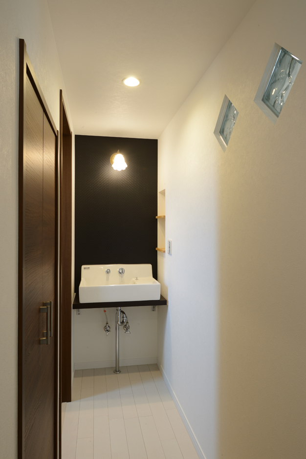 Yamaguchi Design 【収納力、二世帯住宅、間取り】洗面台とトイレが暗くならないよう、廊下の壁にガラスブロックを設け、LDKから明かりをとるように工夫した