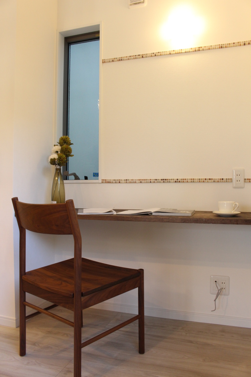 小野田産業～designers house project～｜小さなワークスペースは、シンプルな木製のデスクと椅子が特徴で、壁のアクセントタイルがデザインを引き立てている。