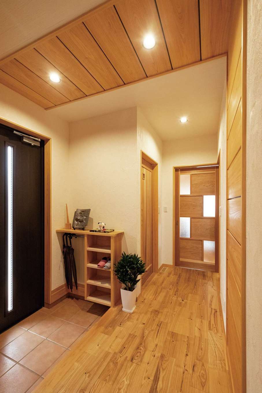 藤田工務店【二世帯住宅、自然素材、間取り】玄関ホールの天井から壁に続く木を使った意匠は、モデルハウスをお手本に。スリッパラックと傘掛け収納は造作で