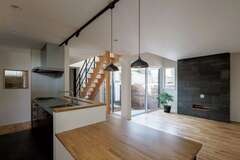 木のぬくもりと北欧テイストが調和したジャパンディスタイルのLDK。ダイニングテーブルをキッチンと一体化させたことで、リビングを広く使えるようにした。キッチンに立つと、家族がどこにいても見えるので安心して料理ができる。南側に隣家があるので日当たりが難しかったが、建物をコの字型に配置して、中庭と階段上の吹抜けから光を取り込めるように設計した