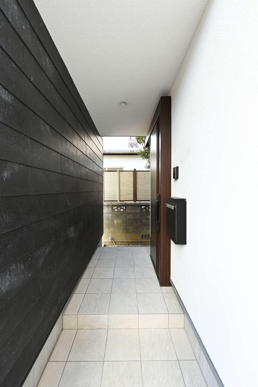 トーリンホーム【デザイン住宅、子育て、間取り】黒い塀の裏面の壁面も表面と同素材で統一。ポーチの奥行き感がいっそう強調され、壁の風合いが上質で洗練された雰囲気を醸し出している