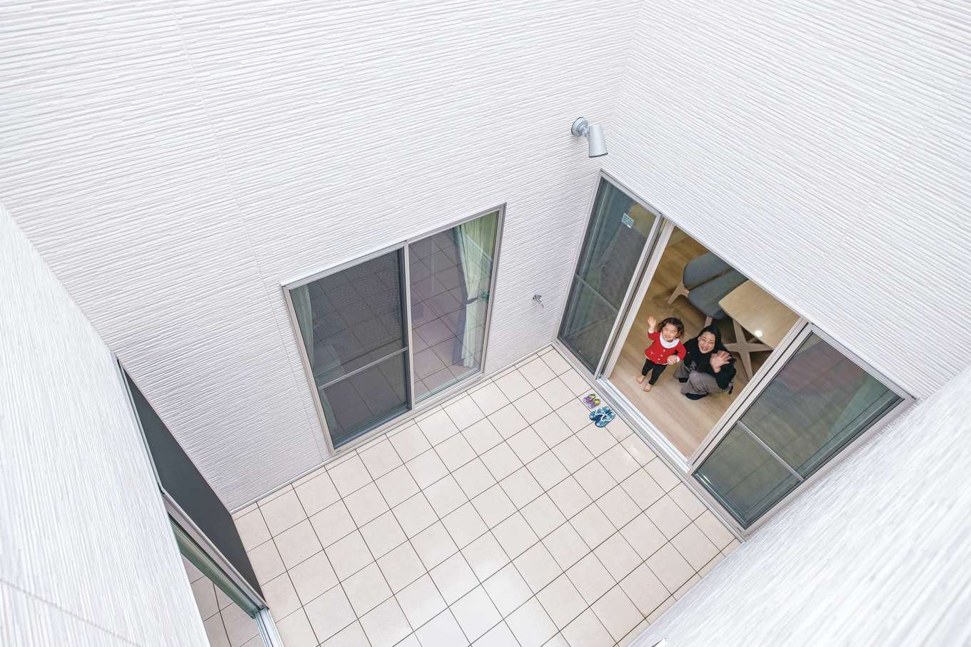 アフターホーム【1000万円台、デザイン住宅、子育て】外部からの視線を気にせず、外遊びができる中庭。今はシャボン玉に夢中な子どもも、夏のプール遊びが待ち遠しい様子。２階の母世帯も同じ間取りなので、「ばぁばー！」「はぁい！」と手を振り合い、コミュニケーションの場にもなっている。また、通風や採光の面でも大いに活躍。白いタイル貼りにしたことで、屋内にはより明るい光が入る