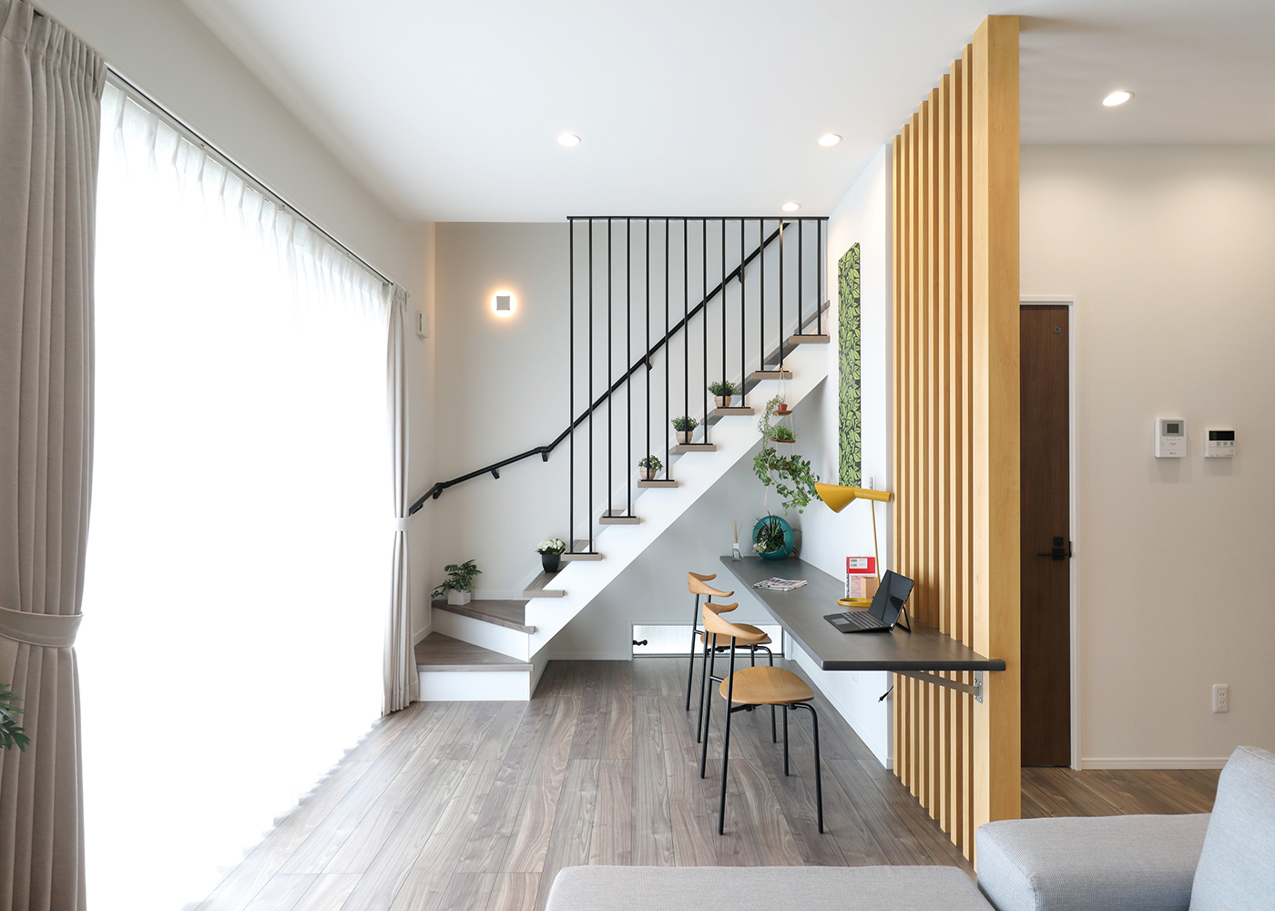 丸昇彦坂建設【デザイン住宅、和風、間取り】格子のパーテーションの前にはスタディコーナーを設置。リビング階段と合わせてアイアンの椅子や無機質なグレーの塗装のカウンターを採用した。LDKの一角にカフェのような空間が生まれたことで、生活に彩りが加わる。コーヒータイムなどにも活躍しそう