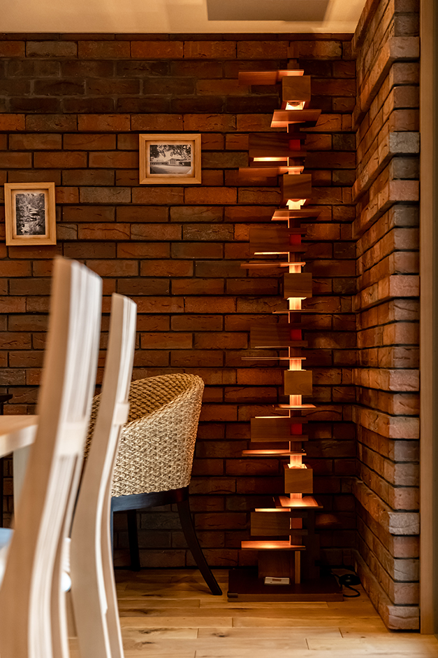 住宅工房 アリアンス【富士市伝法2001-35・モデルハウス】ライトの名作であるフロアーランプの「タリアセン 2」。幾つものチェリー材のブロックで構成され、それぞれに白熱電球が組み込まれている。計算されたデザインにより、木目と木漏れ日の光が美しく調和し、暖かくムーディーな空間を演出する