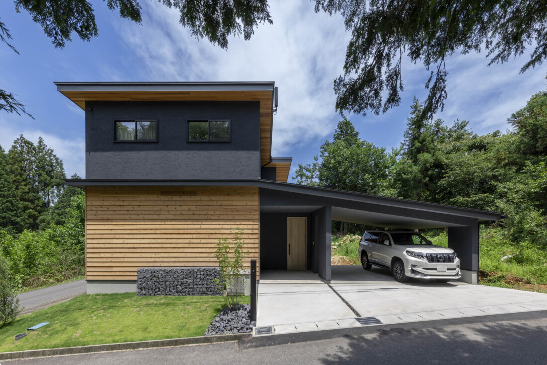 チェックハウス｜ダークな外壁に木材をアクセントにしたモダンな外観。車が収まるビルドインガレージが特徴で、機能性とデザイン性を両立している。