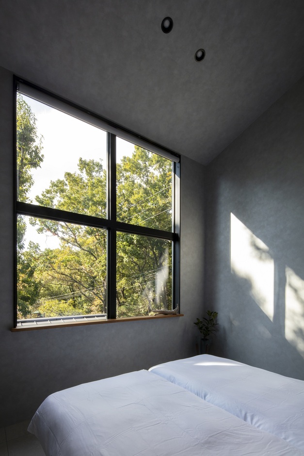 大きな窓から自然光が差し込む明るい寝室。シンプルで落ち着いたインテリアが特徴で、外の景色を楽しめるリラックス空間である。