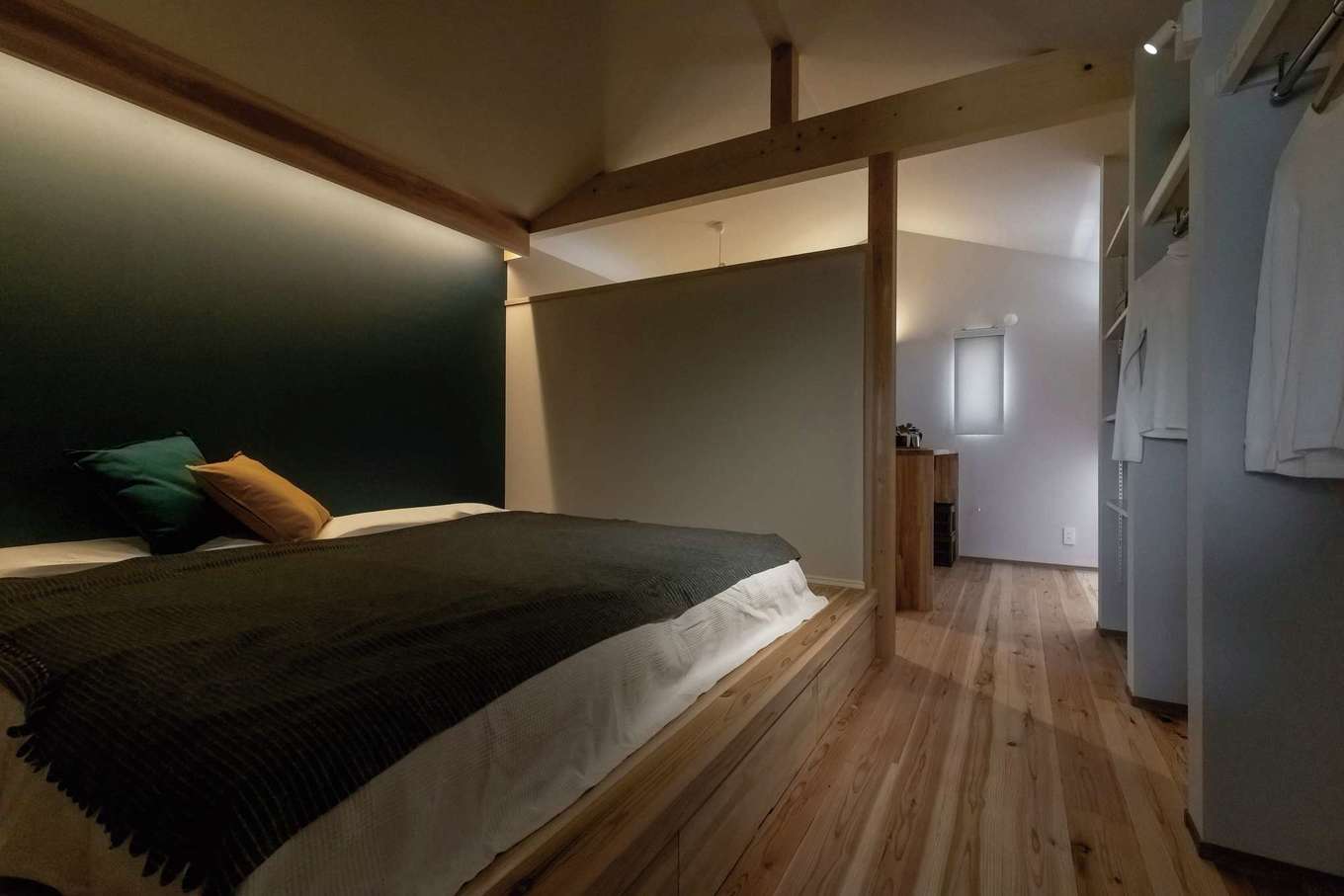 住まいるコーポレーション｜2階の主寝室は以前夫婦で泊まった京都のホテルをイメージして、やや暗めのスタイリッシュな仕上がりに。ベッドは造作で、小上がりの部分は収納スペース。隣室の畳コーナー、趣味部屋と間仕切りなしでつながっているので、適温の空気が循環する