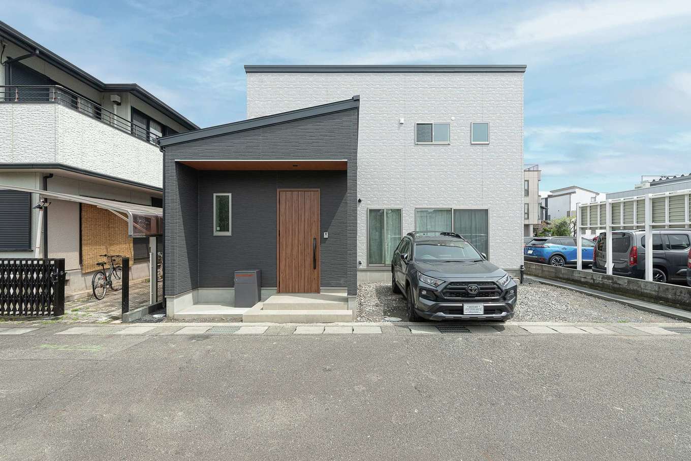 三和建設【デザイン住宅、子育て、間取り】濃淡のあるグレーの壁に、木調の玄関ドアでアクセントを付けた外観