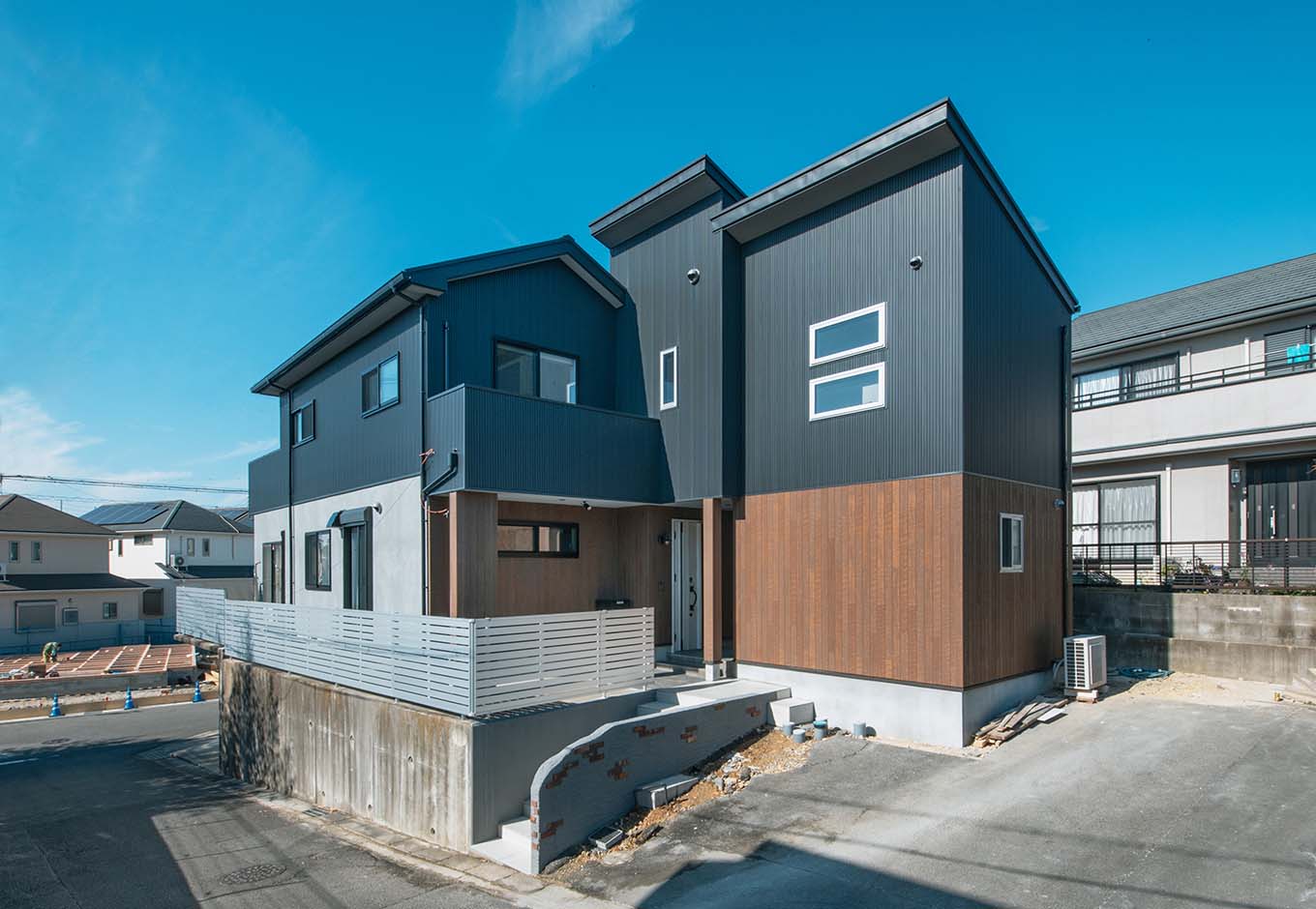 ハート住いる｜ガルバリウム鋼板、サイディング、塗り壁といった異素材ミックスで仕上げた、シンプルモダンな外観デザイン。増築した右端部分が将来の親世帯になり、左側の子世帯とつながっている。コンクリート造ガレージは既存のまま活用
