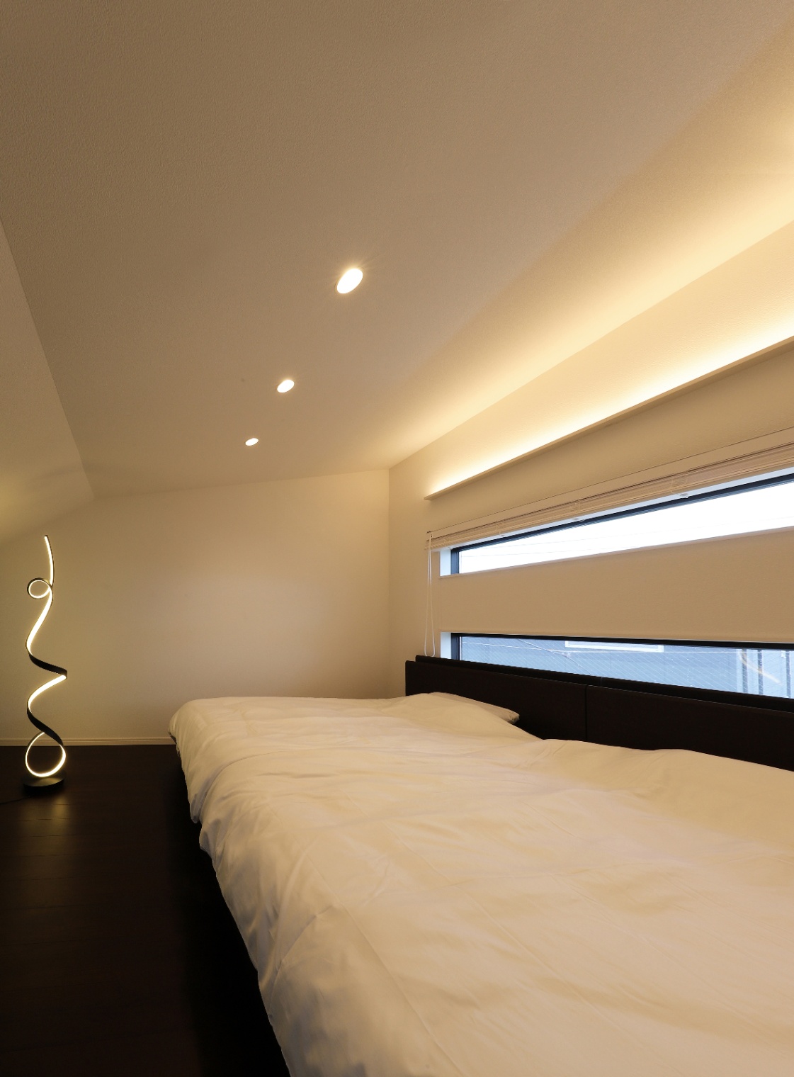 アイダ設計　｜ミニマルデザインの寝室。シンプルで広々とした空間に、間接照明が柔らかく光り、リラックスした雰囲気を醸し出している。