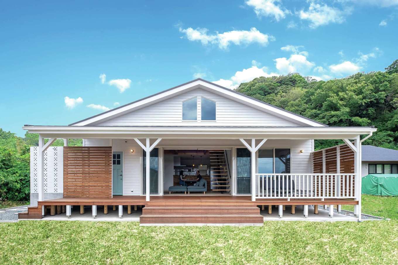富士ホームズデザイン【デザイン住宅、趣味、平屋】白く塗られた板張りの外観が“本場感”を演出し、のどかな景色になじむ。ウッドデッキにかかるひさしは室内からの眺めにも配慮しながら、角度と長さが丁寧に吟味された