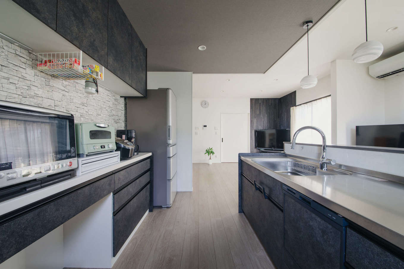 エフエフ住宅【ペット、平屋、スキップフロア】下がり天井を採用し、リビングとゾーン分けしたキッチンスペース。キッチンのバックヤードにはゴミ箱が置けるカウンター収納を設けた。カウンターの上に電化製品を並べることで調理もスムーズに行える