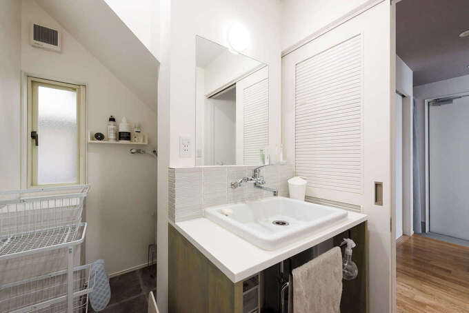 玄関から直行できる洗面脱衣所。階段下のスペースを洗濯機置き場にして、広い空間を確保。タイル貼りのシンプルな洗面台は造作で実現