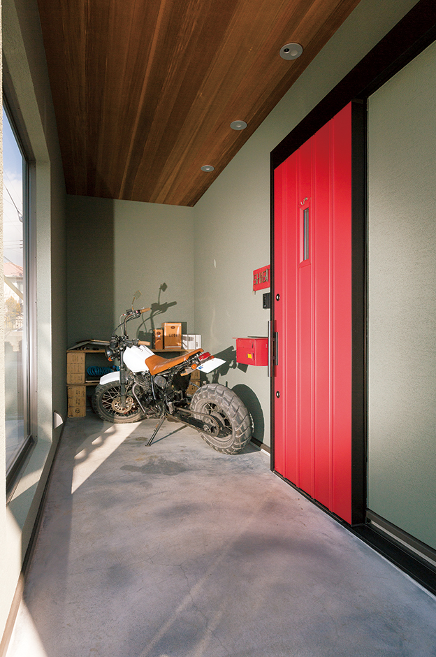 富士ホームズデザイン【デザイン住宅、子育て、インテリア】緑の塗り壁に赤いドアが映える玄関ポーチ。木張りの天井と墨を混ぜたモルタル床がいい味を出している