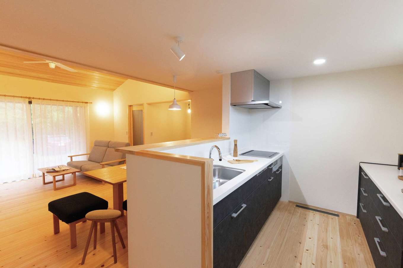 住まいるコーポレーション【自然素材、省エネ、平屋】キッチンからは、ワンフロアの平屋全体を見渡すことができる。手元を隠すために腰壁を高くし、大人が数人入っても窮屈にならないよう広く確保した。リビングと天井高を変えたことで視線が抜け、より広く感じられる