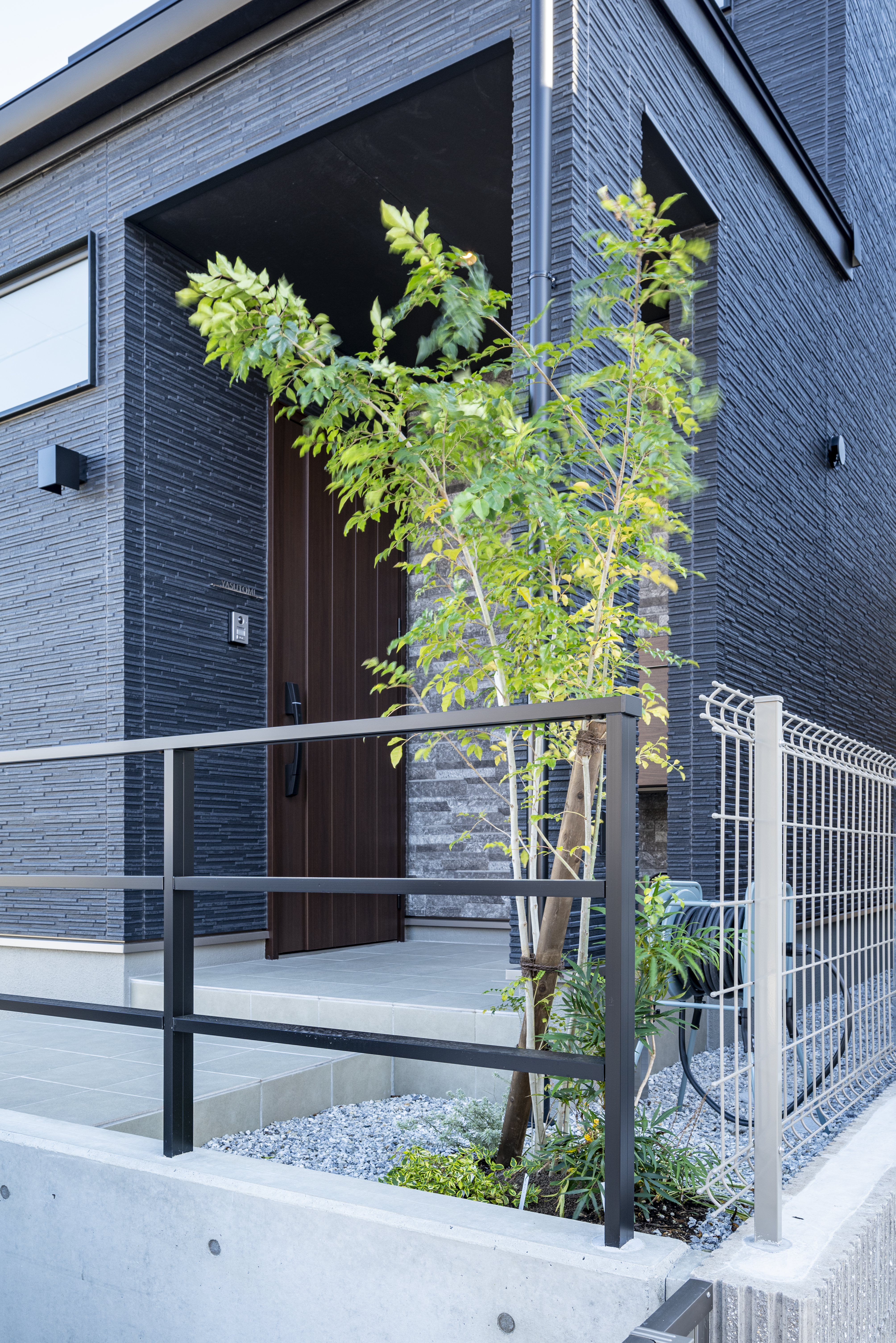 トキワハウス デザイン アンド ビルド（常盤工業）｜シックなブラックの外壁が印象的な現代的な建物の外観。エントランス付近には植栽が施され、自然との調和が感じられる設計。