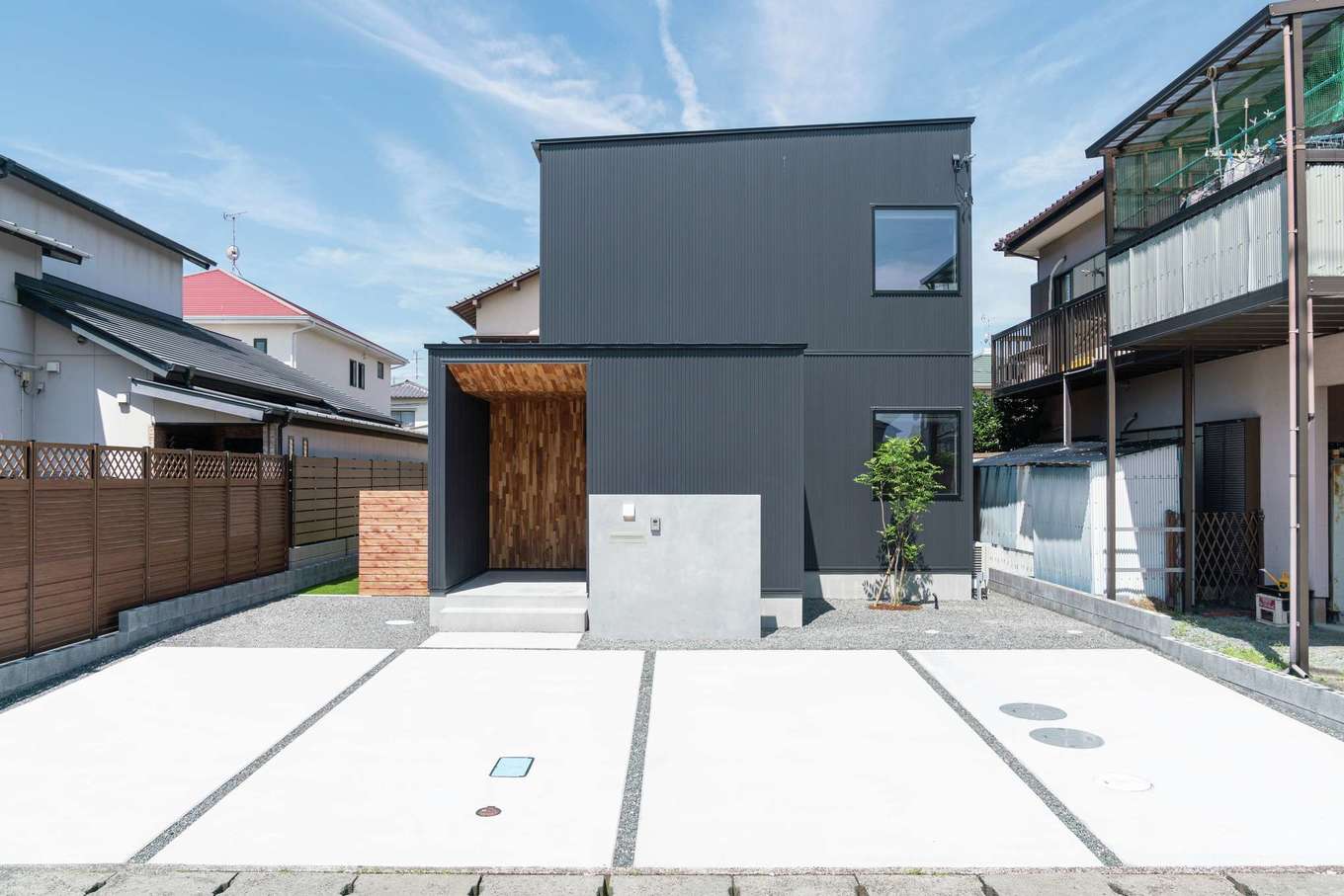 住家 JYUKA【デザイン住宅、ペット、建築家】スタイリッシュなキューブ型の外観デザイン。ブラックのガルバリウム鋼板にポーチの無垢チーク材が程よく調和している。シンボルツリーのシマトネリコは玄関からも見える