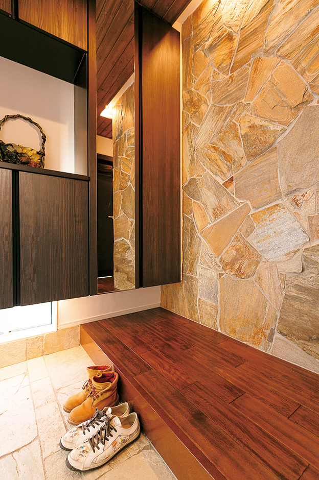 外壁の一部と同じ天然石を張った玄関ホール。ダークブラウンの無垢の床FREDDYとの相性も良く、より高級感がただよう