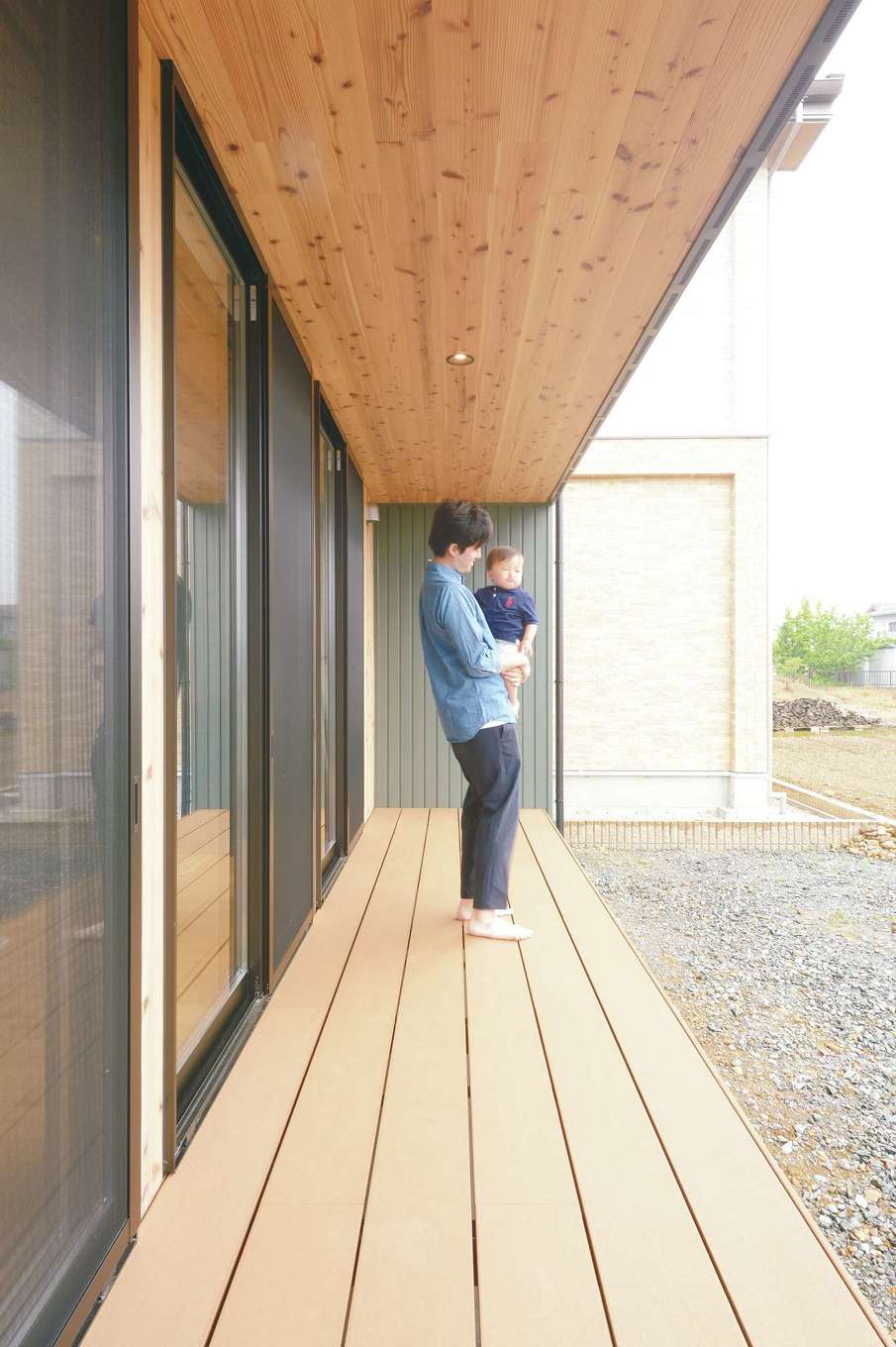 MABUCHI【子育て、間取り、建築家】緑の景色が広がる南面に設けた縁側のような長いウッドデッキ。軒が深いので、直射日光や小雨の影響を受けずに子どもを遊ばせることができる。夏は家族みんなでここに座って、スイカの種を思い切り飛ばしてみたい！