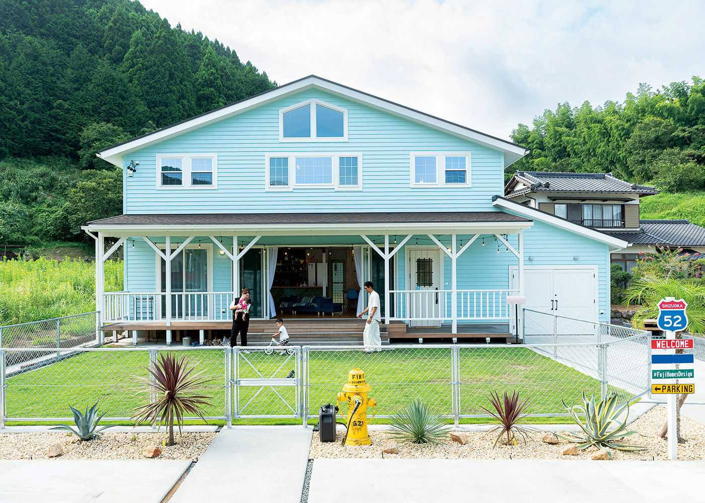 富士ホームズデザイン【輸入住宅、趣味、ガレージ】豊かな緑に大らかな外観が映える。カバードポーチの一角には休憩にピッタリのカウンターを用意。外構も同社に依頼。知人に製作してもらった看板には感謝を込めて同社の社名を記した