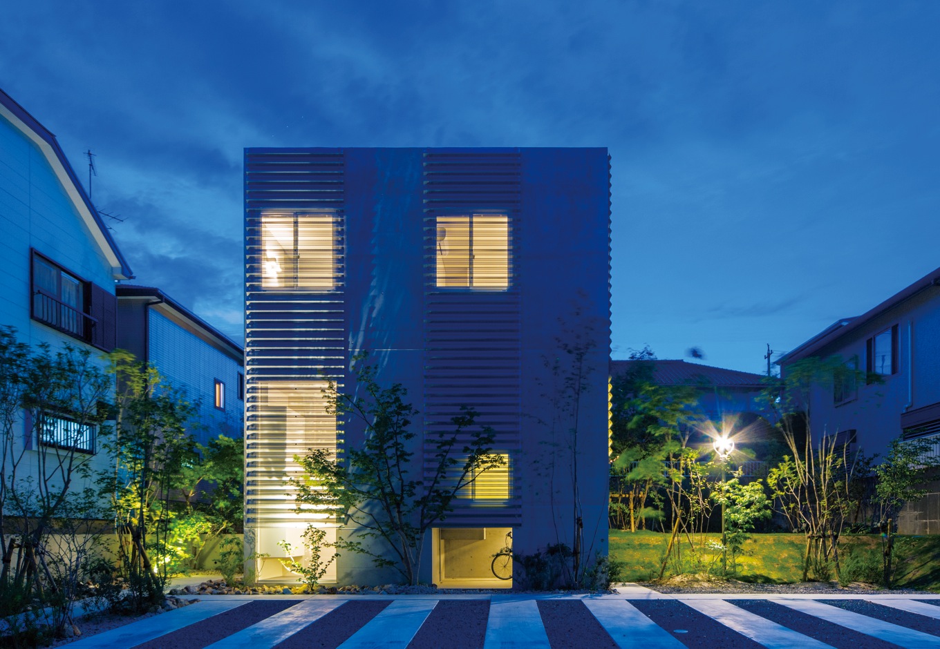 MABUCHI【デザイン住宅、建築家、鉄骨鉄筋コンクリート構造】図書館などに使われる「有孔折板」を採用し、外からの視線を遮りつつ、光と風を招き入れる。ライトアップされた外観フォルムは街の風景の一部となる