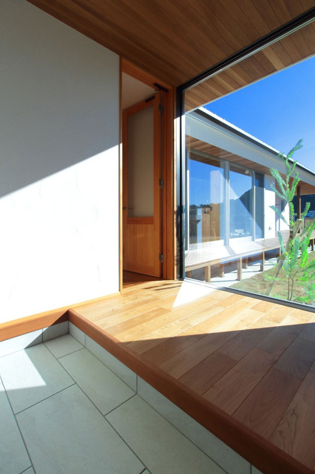 アイジースタイルハウス【デザイン住宅、建築家、平屋】玄関に入って正面にも大きな窓を配置。足を踏み入れた瞬間、庭とシンボルツリー、そして奥へと広がる野山の緑がダイレクトに癒しを運ぶ